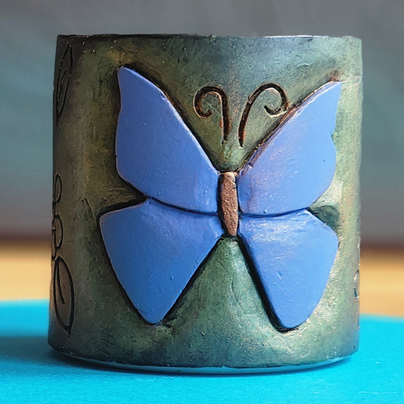Cylindrical container with a blue butterfly design on a WAX surface