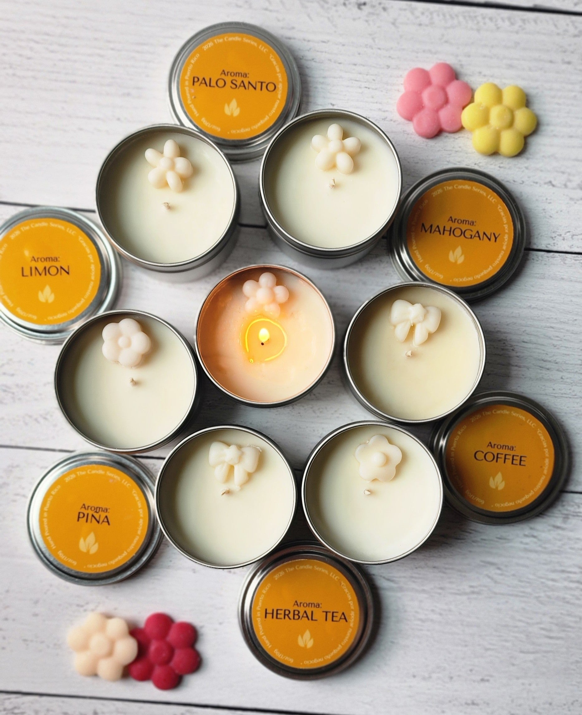 Assorted candles in 6oz tins with visible flames on a wooden surface